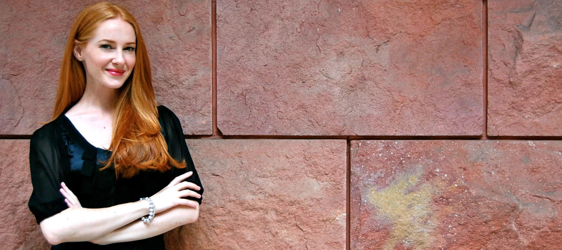 Joanna Campbell, founder of Show + Tell Social, standing in front of a red stone wall